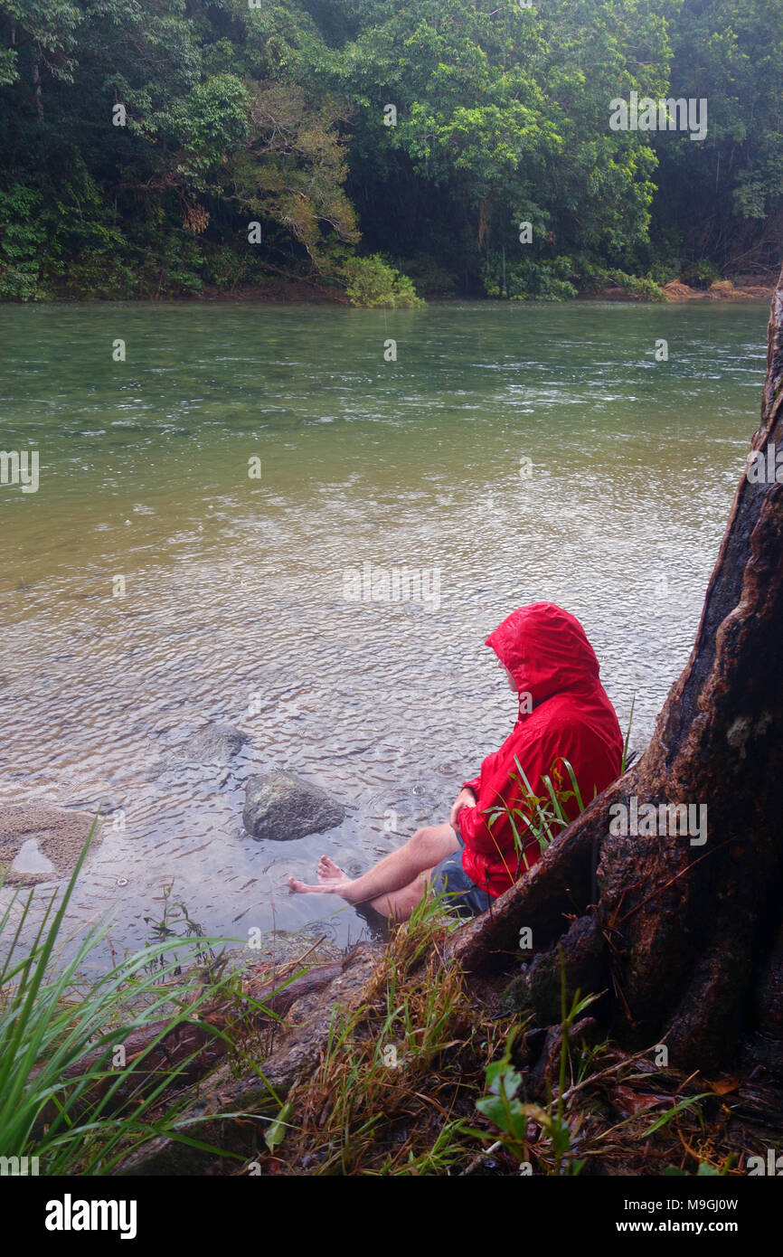 Mann sitzt auf der Bank von Mulgrave Fluß während der Regenzeit, Goldsborough Valley, in der Nähe von Cairns, Queensland, Australien. Keine MR Stockfoto