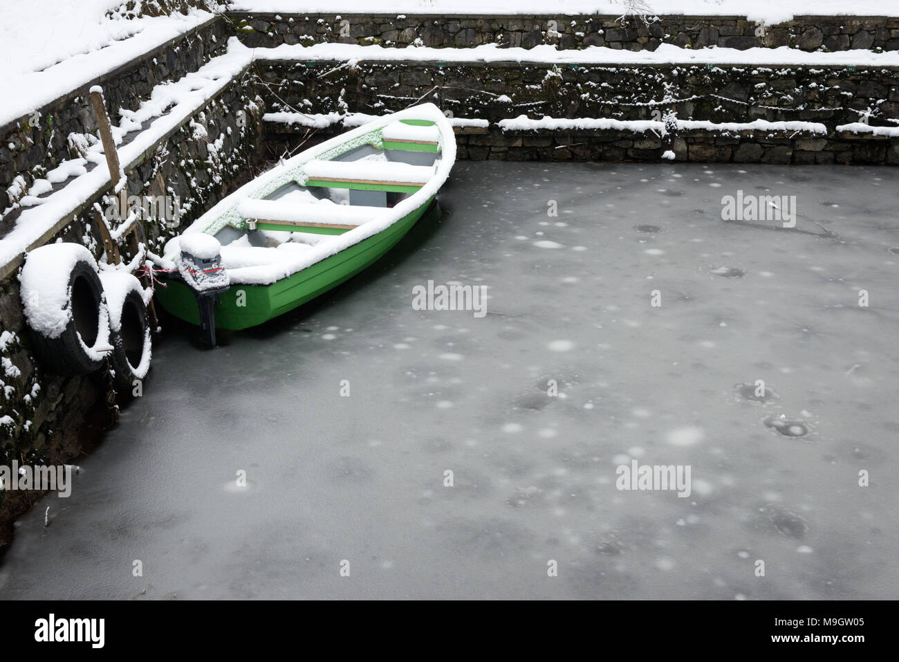 Grünes Fischerboot, das in gefrorenem Wasser festgemacht ist. Heftiger Schneefall im Killarney National Park, County Kerry, Irland ab März 2018 Stockfoto