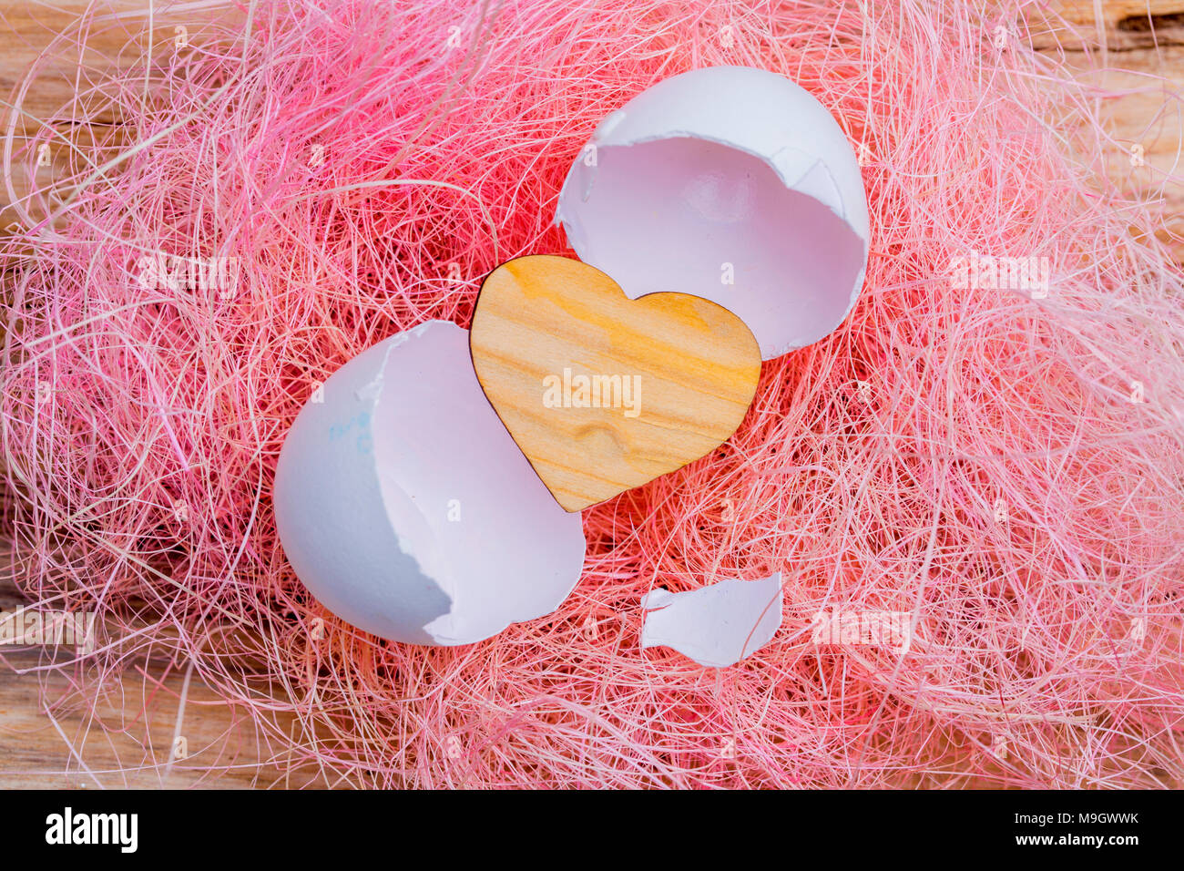 Kleine hölzerne Herz aus einem weißen Ei geschlüpft. Rosa Hintergrund Stockfoto