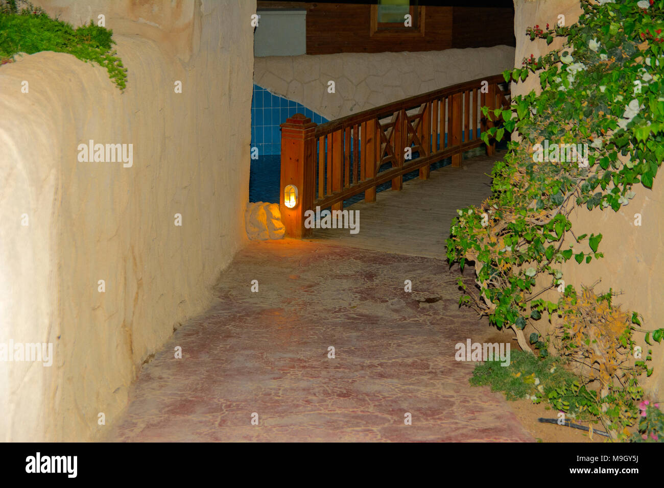 Sharm-el-Sheikh, Ägypten - März 14., 2018. Eine schöne hölzerne Brücke zwischen Pools mit klarem, blauem Wasser und eine Reflexion von Objekten in es in der Nacht. Cyr Stockfoto
