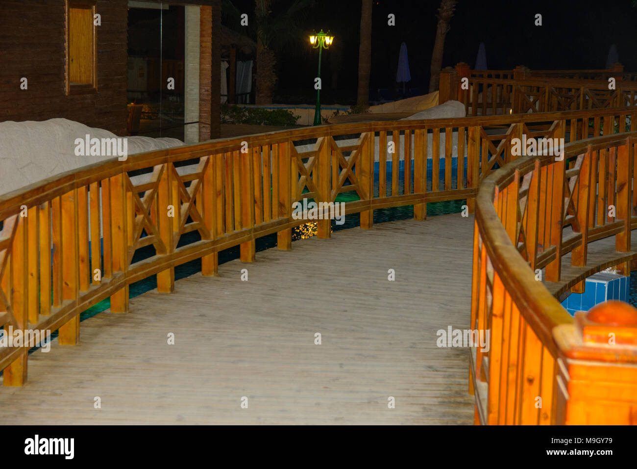 Sharm-el-Sheikh, Ägypten - März 14., 2018. Eine schöne hölzerne Brücke zwischen Pools mit klarem, blauem Wasser und eine Reflexion von Objekten in es in der Nacht. Cyr Stockfoto