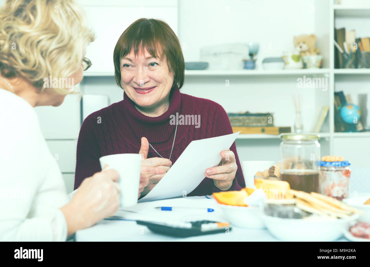 Zwei positive reife Frauen, die Papiere beim Sitzen auf Küche Stockfoto