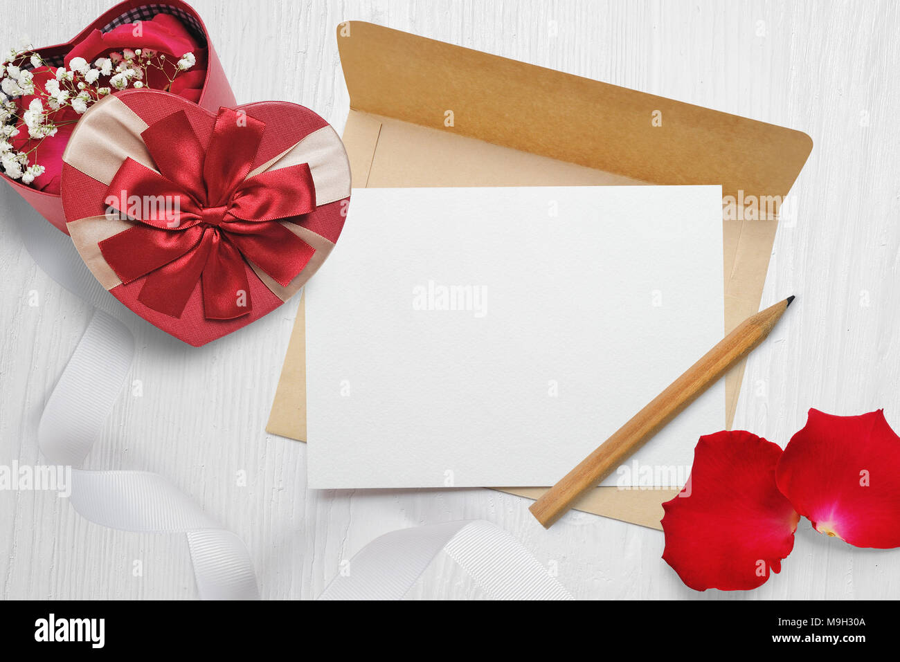 Mockup Kraftpapier Umschlag und einen Brief mit einer herzförmigen Geschenk mit roter Schleife und Rosenblättern, Grußkarte für Valentines Tag mit Platz für Ihren Text. Flach, Ansicht von oben Foto Mock up Stockfoto