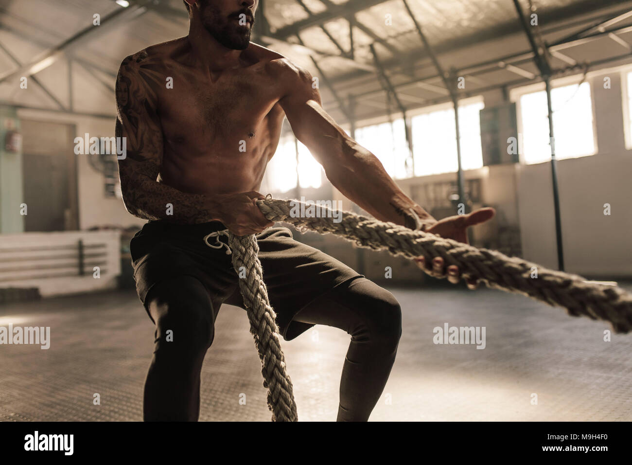 Männlichen Bodybuilder ziehen Seil Cross Training Gym. Männliche Athlet Übungen mit Seil im Fitnessstudio. Stockfoto