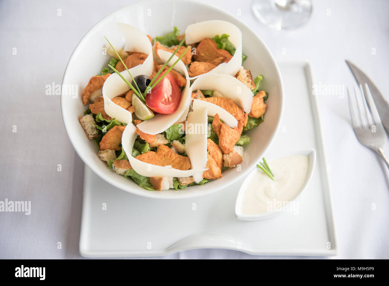 Ein Aus-dem-top Foto von einer schönen Huhn und grünen Salat. garniert mit schönen Käse. Weiße Platten und weiße Tischtuch zu der Eleganz. Stockfoto