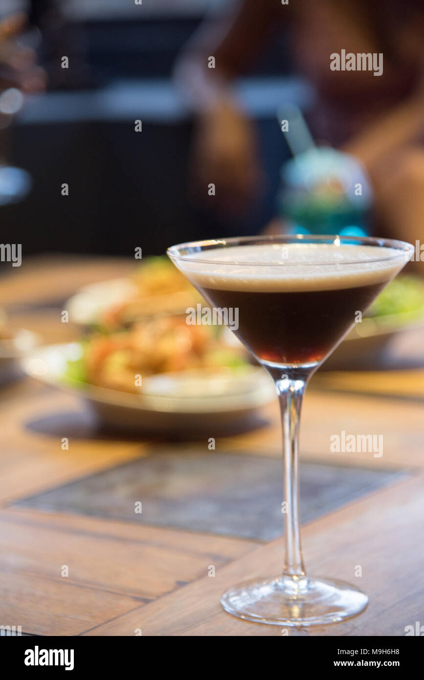 Eine Chocolate Martini sitzt auf einem Stehtisch mit unscharfen Essen im Hintergrund. Stockfoto