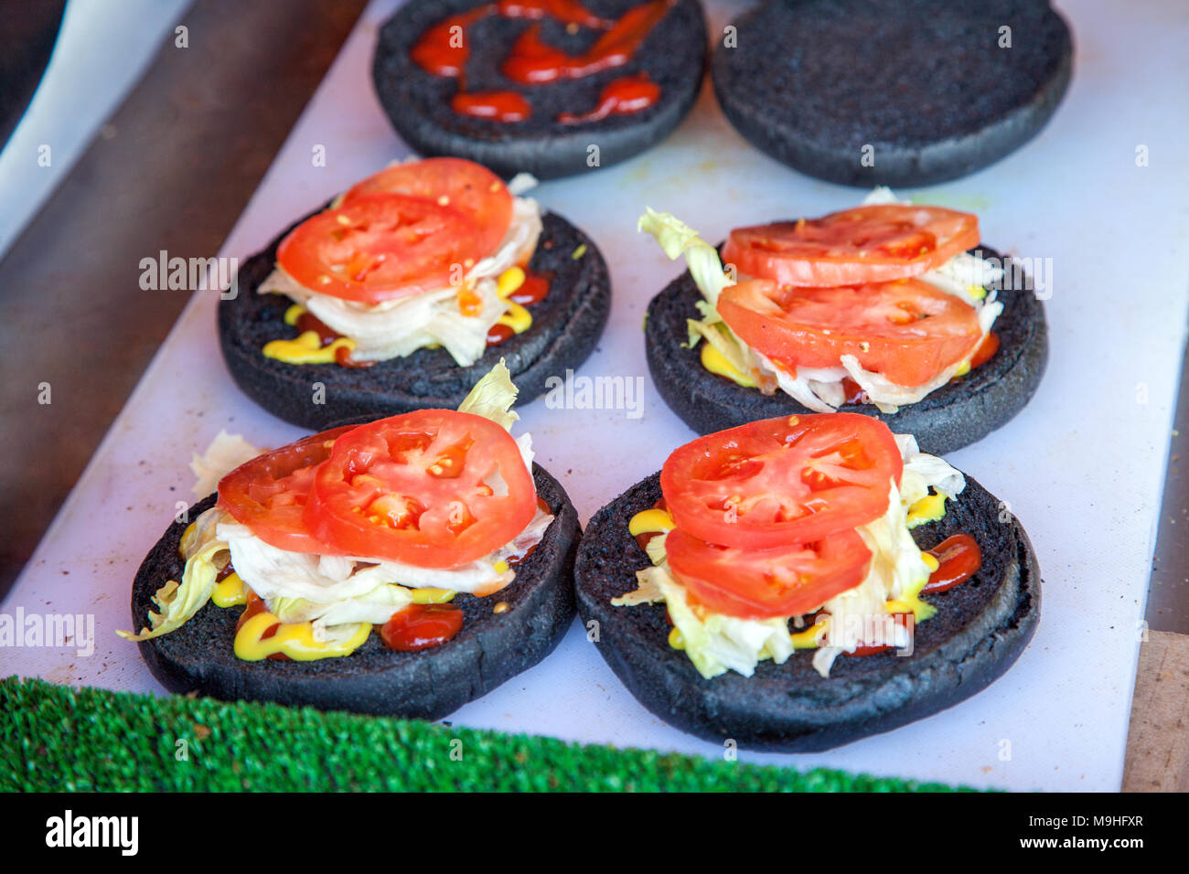 Brötchen mit Tomaten und Kohl mit Ketchup und Senf auf weiße Oberfläche, Vorbereitung von schwarzen Burger Konzept Stockfoto