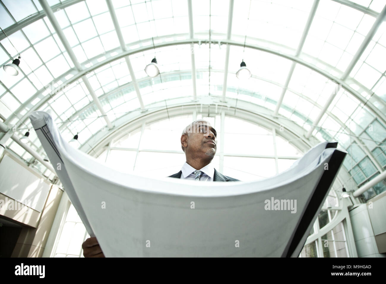Low Angle View, ein Mann mit einem großen Dossier der Baupläne oder Blaupausen, unter einer Glaskuppel, im Atrium oder im Büro, Architekt Stockfoto