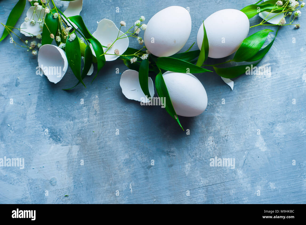 Stiftleiste mit rohen Eiern, dekorative grüne Blätter und Blumen. Moderne Ostern Konzept mit kopieren. High Key konkreten Hintergrund. Stockfoto