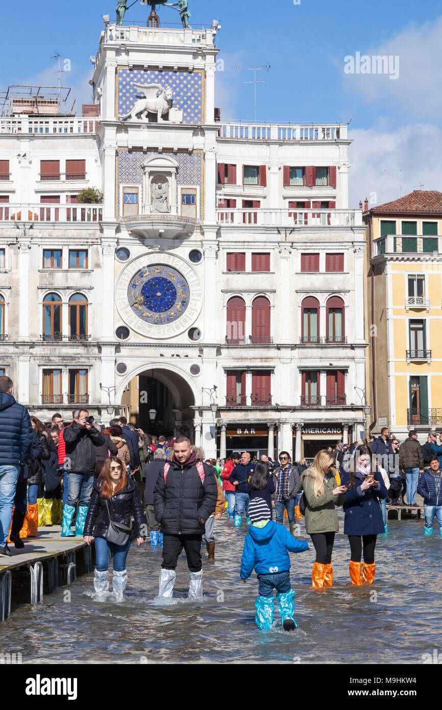 Touristen das Waten durch Acqua Alta Flut vor dem Glockenturm in Piazza San Marco (Markusplatz), Venedig, Venetien, Italien in bunten Plas Stockfoto