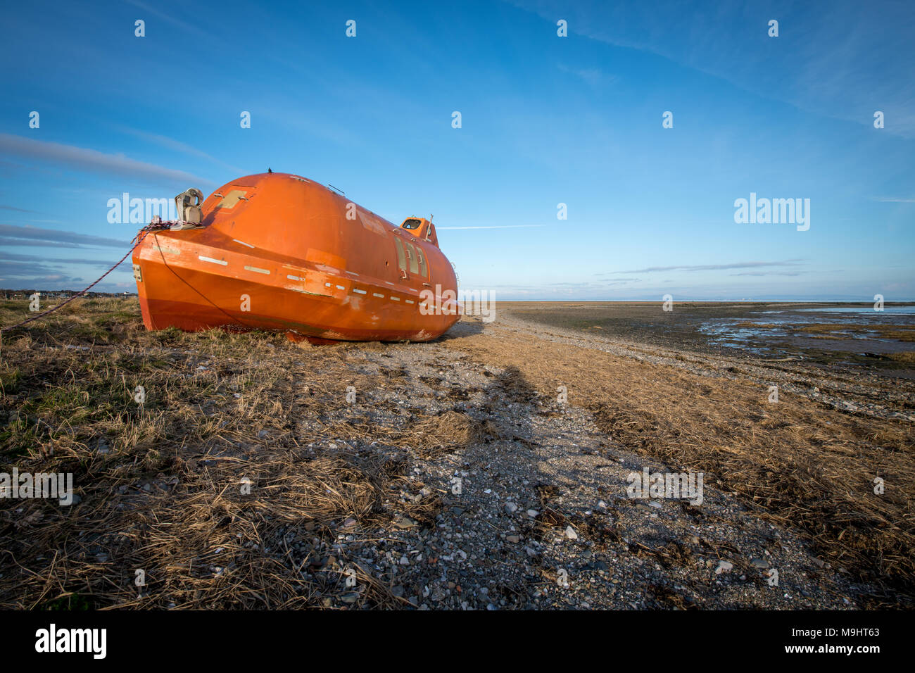 Eine alte, verlassene, orange Leben Boot links am Strand zwischen Rampside und Roa in der Nähe von Barrow-in-Furness, Cumbria. Stockfoto