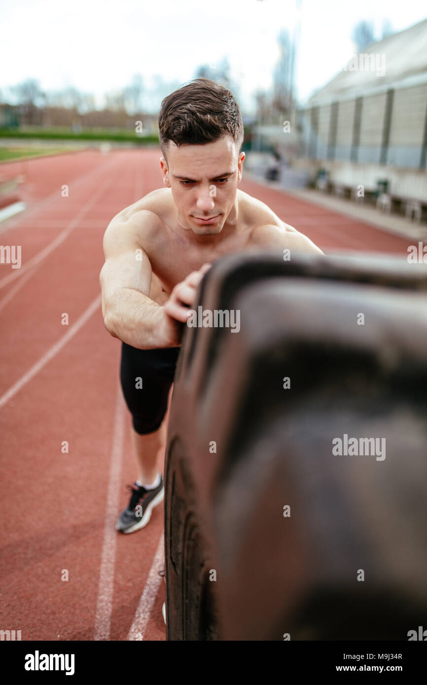 In der Nähe der Jugendlichen muskulösen Mann spiegeln eine riesige Reifen für Training Muskeln an der Tartanbahn auf dem Stadion. Stockfoto