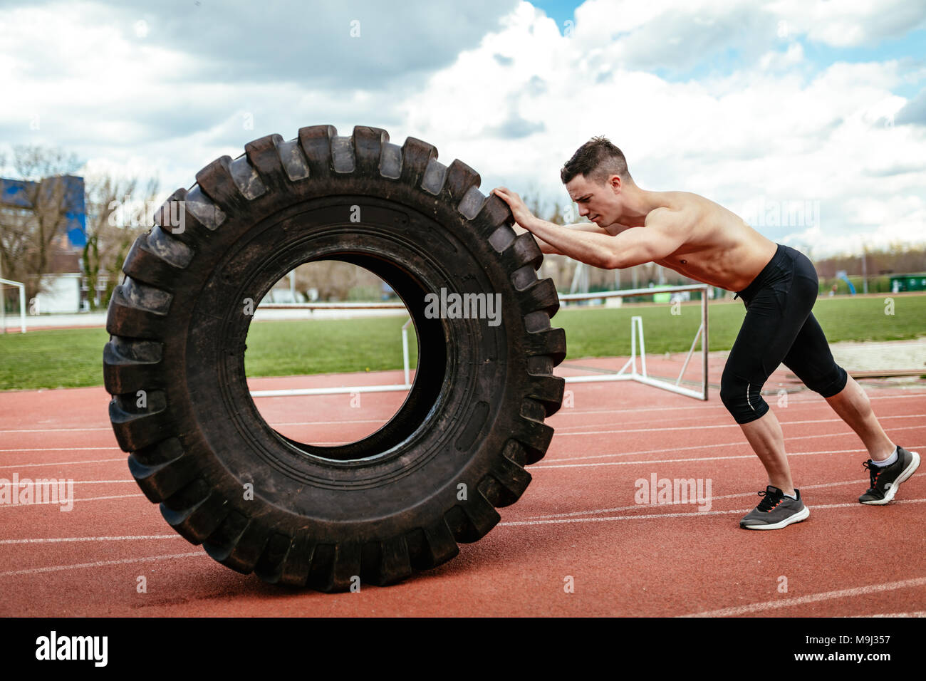 Junge muskulöse Mann spiegeln eine riesige Reifen für Training Muskeln an der Tartanbahn auf dem Stadion. Stockfoto