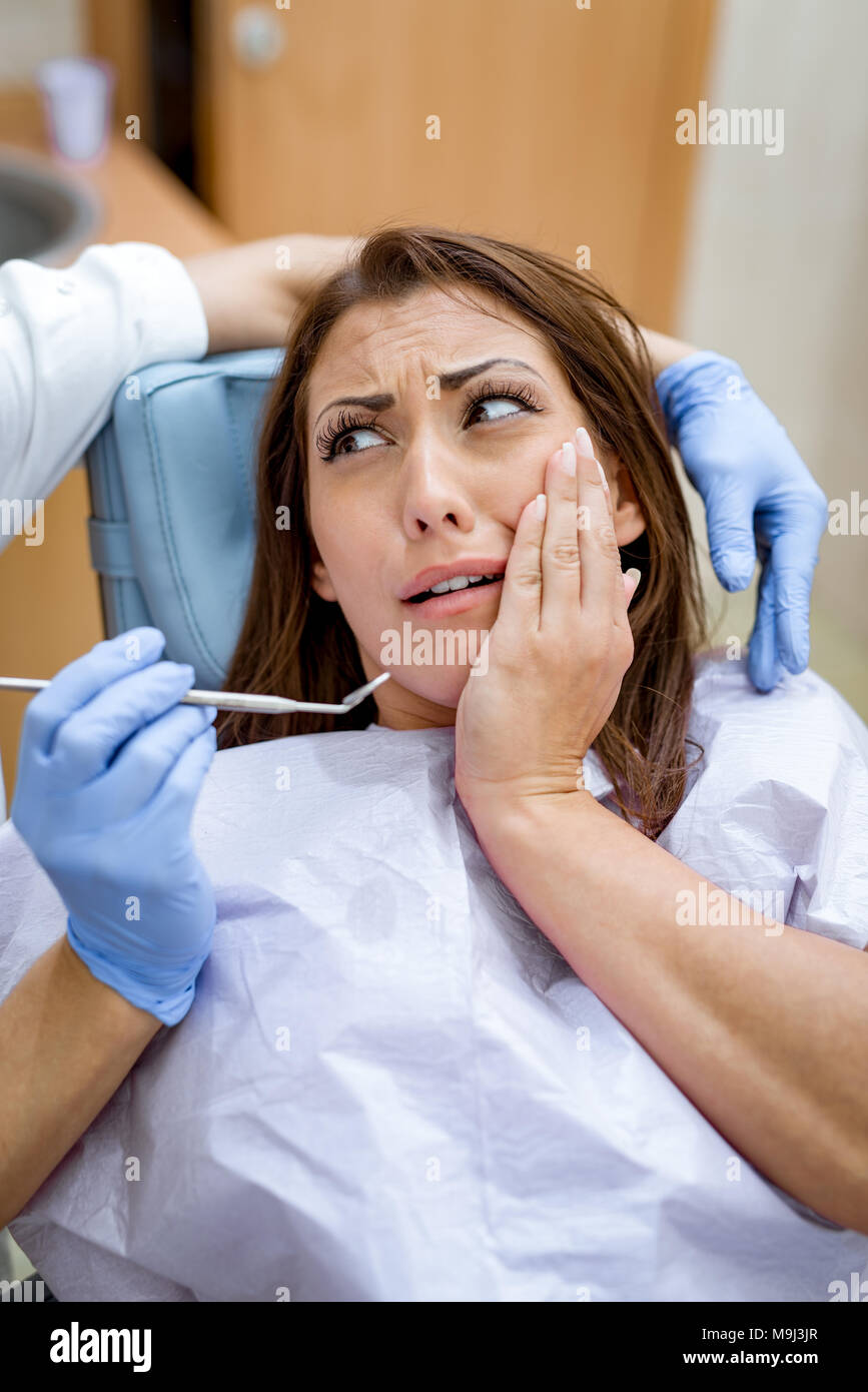 Schöne junge Frau zu Besuch beim Zahnarzt Büro mit Zahnschmerzen, die Hand über den Mund in Angst. Stockfoto