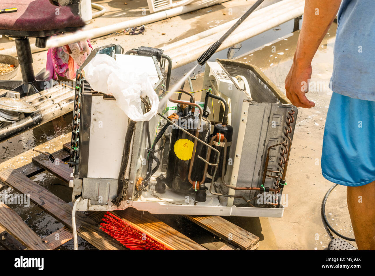 Einen professionellen Elektriker ist die Reinigung der Fenster Klimaanlage auf dem Dach eines Hauses mit seinem hohen Druck Wasser Pistole und trägt blaue Shorts Stockfoto