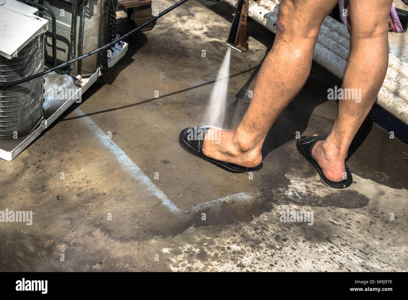 Einen professionellen Elektriker ist Waschen seinen Fuß nach der Reinigung der Fenster Klimaanlage auf dem Dach eines Hauses mit seinem hohen Druck Wasser Pistole Stockfoto
