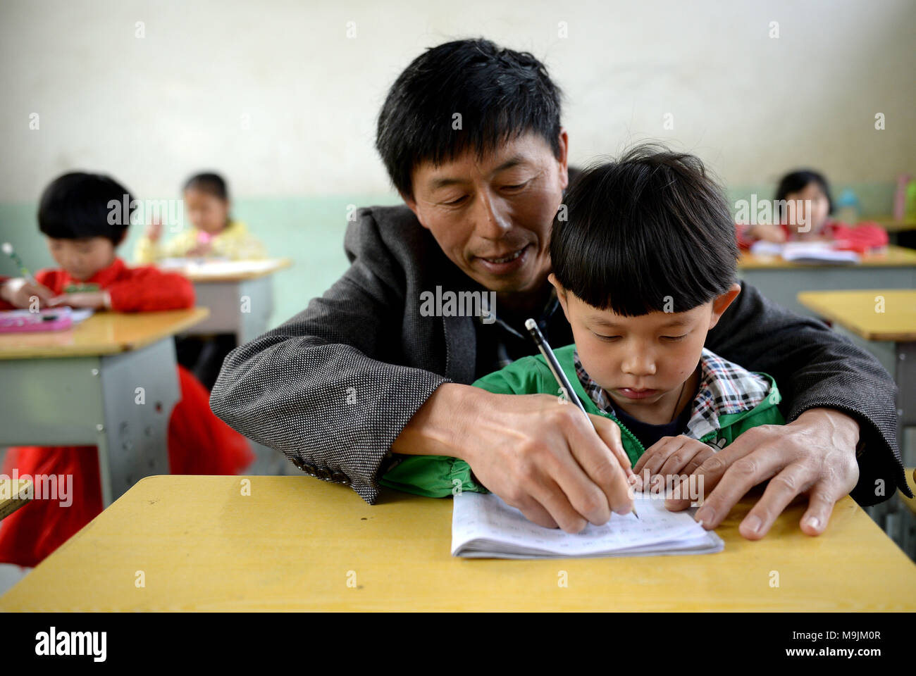 (180327) -- PINGLI, 27. März 2018 (Xinhua) - Lehrer ihr Shiping lehrt ein Schüler in der Schule in Xihe Stadt Pingli Grafschaft zu schreiben, in der Provinz Shaanxi im Nordwesten Chinas, 26. März 2018. Ihr Shiping, 53 Jahre alt, entschieden, hinter am Renjiaya Grundschule als Lehrer mit seiner Frau als die Zahl der Studenten, die hier wohnen, auf nur 15 gesunken. Die Schule, die in abgelegenen bergigen Gegend, 30 Kilometer von der Grafschaft. Mit der Verringerung der Bevölkerung, Ihr und seine Frau die Einzigen zwei Lehrer in der Schule. Die Pflege ihrer Studierenden, die Paare bestimmt Dev Stockfoto