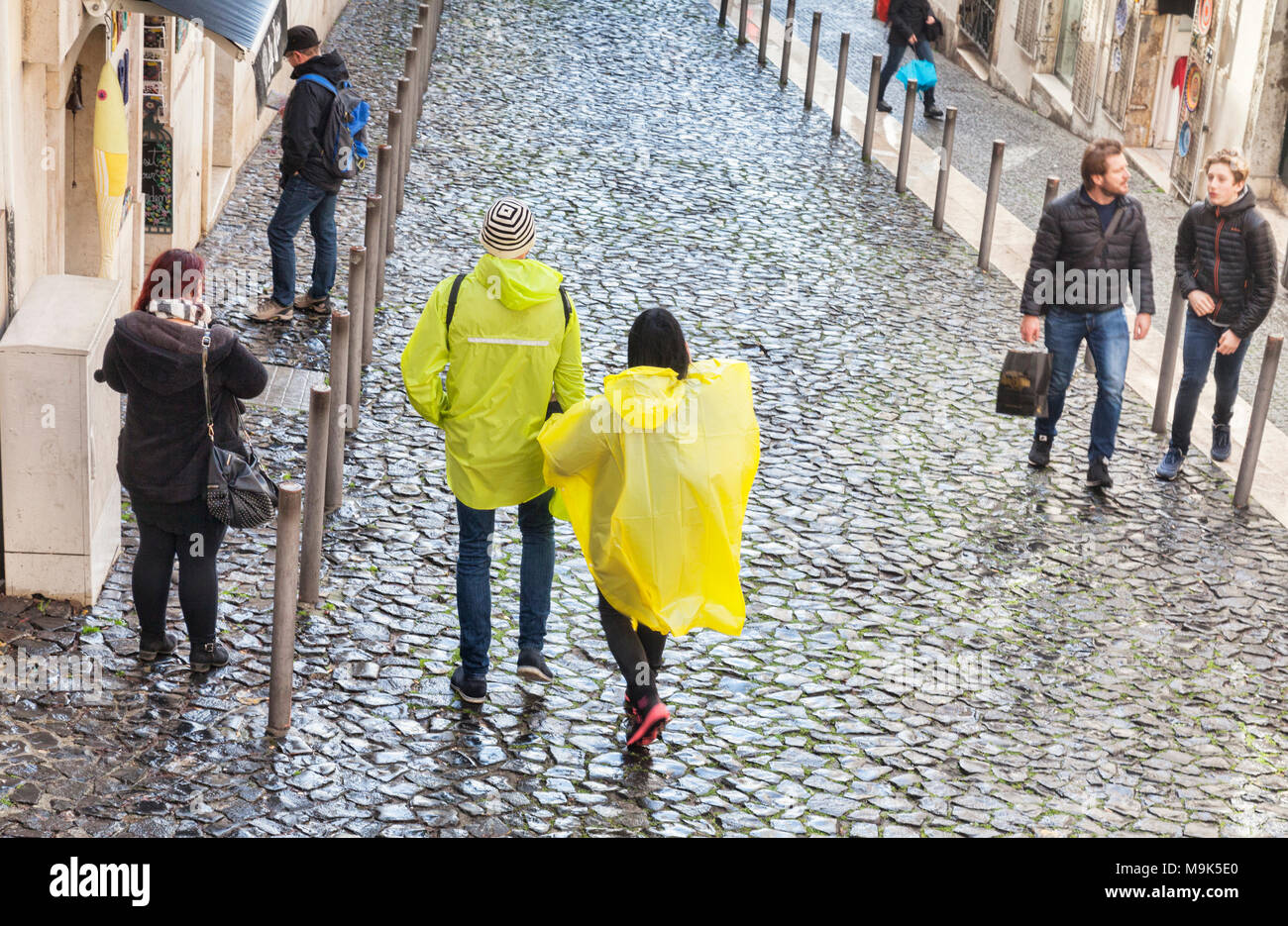 1. März 2018: Lissabon Portugal - Paar tragen gelbe Kunststoff Regencapes in der Altstadt von Lissabon an einem regnerischen Tag. Stockfoto