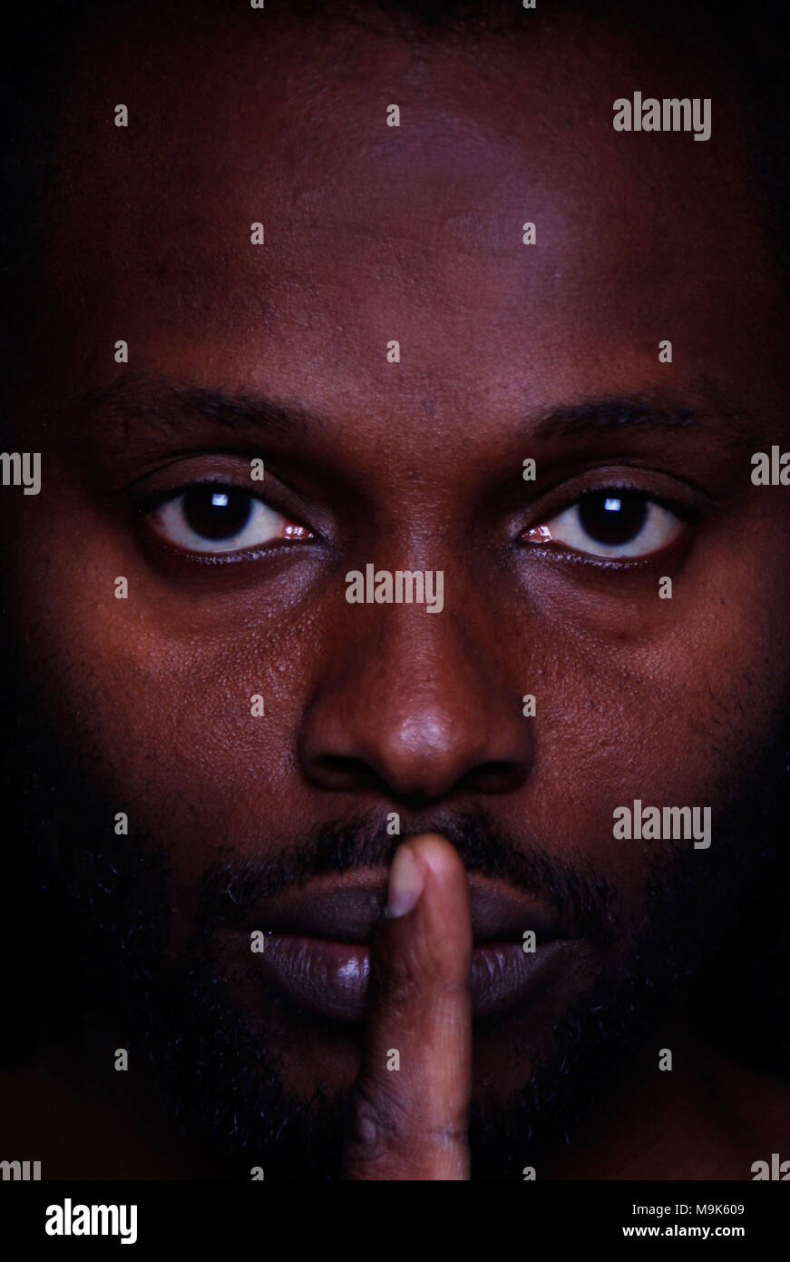 Ein Bild von einem afrikanischen Mann an Sie mit einem Finger über seine Lippen Stockfoto