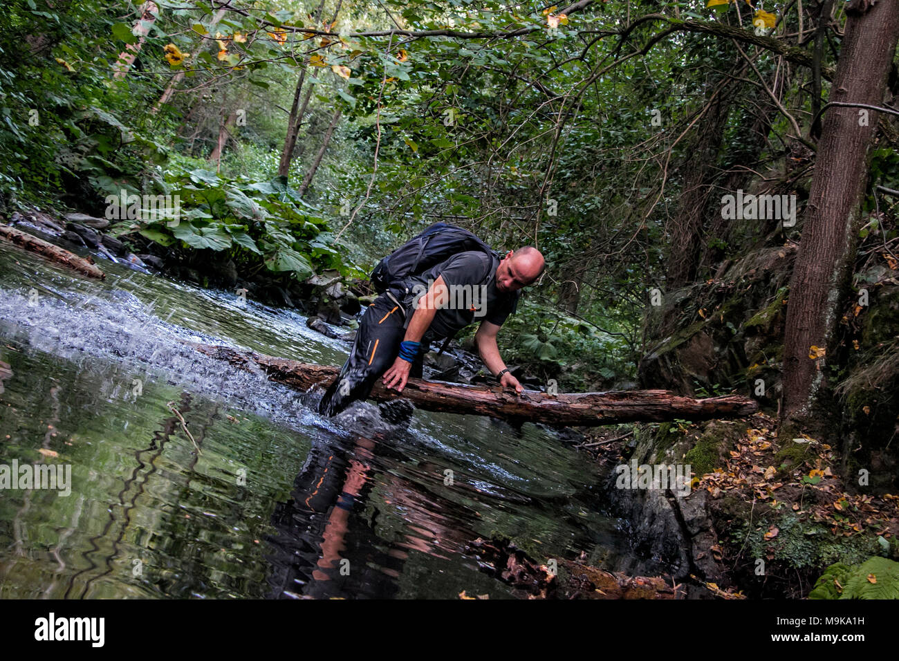 Ein Mann ist das Springen über eine Holz Anmelden beim durchqueren eines Flusses. Konzept des Überlebens in der Wildnis. Mаn vs wild. Stockfoto