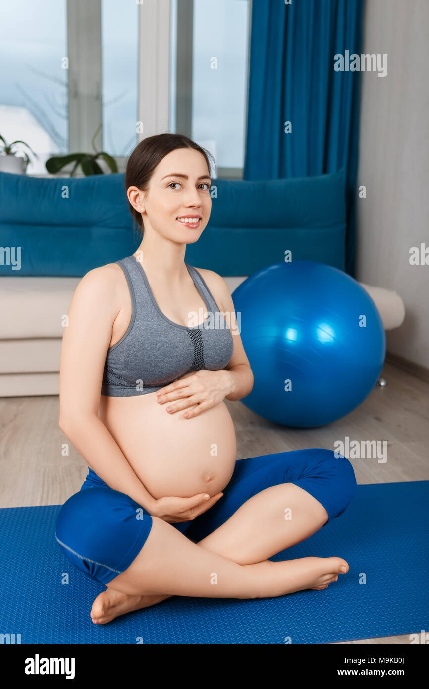 Gerne schwangere Frau mit Fit Ball zu Hause. Die werdende Mutter ihr Bauch berühren. Schwangerschaft, Gymnastik für Schwangere, gesunden Lebensstil Konzept Stockfoto