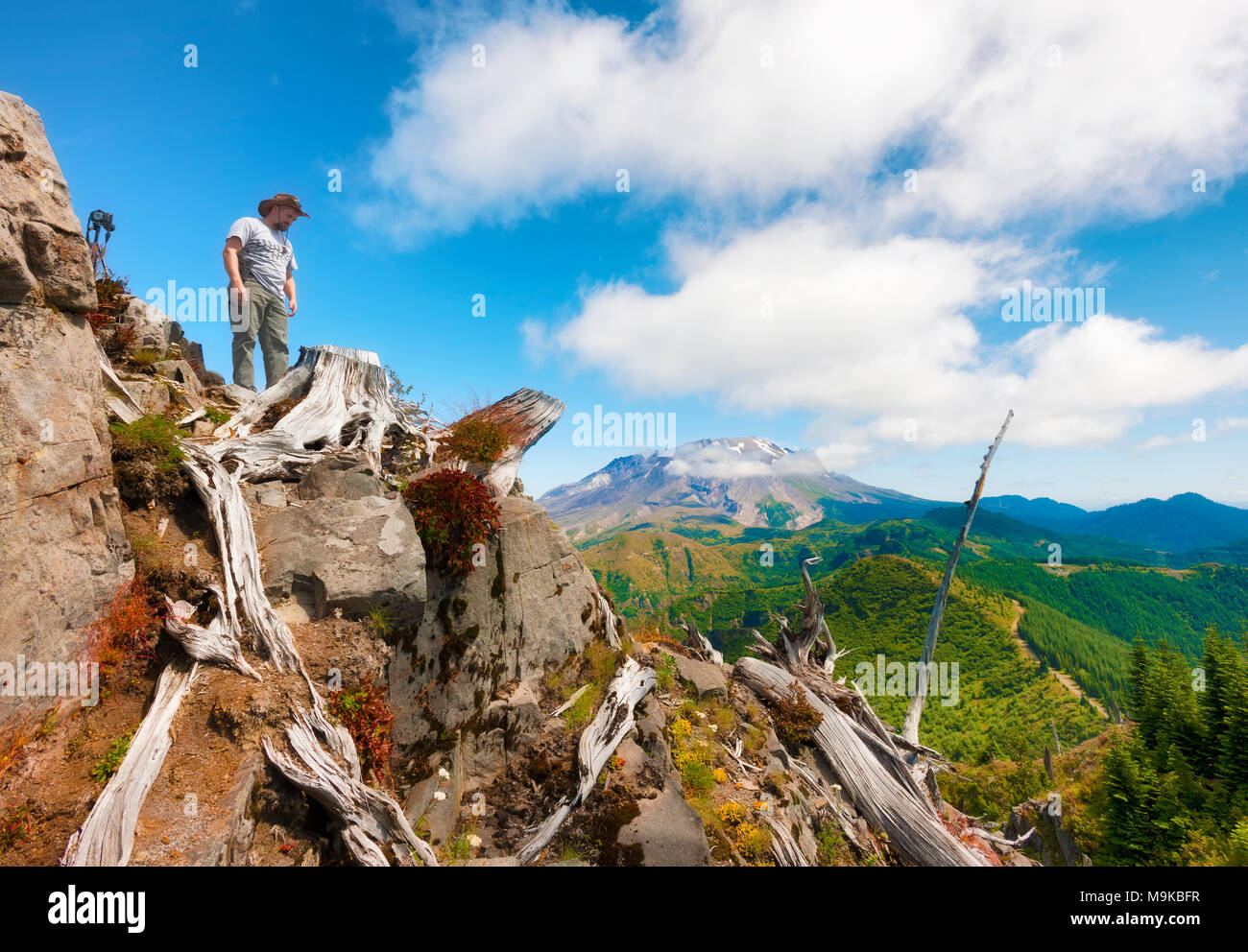 Ein Wanderer/Fotograf schaut von oben auf Castle Peak, seine Kamera und Stativ in der Nähe mit Mt. St. Helens im Hintergrund in Gifford Pinchot Na Stockfoto