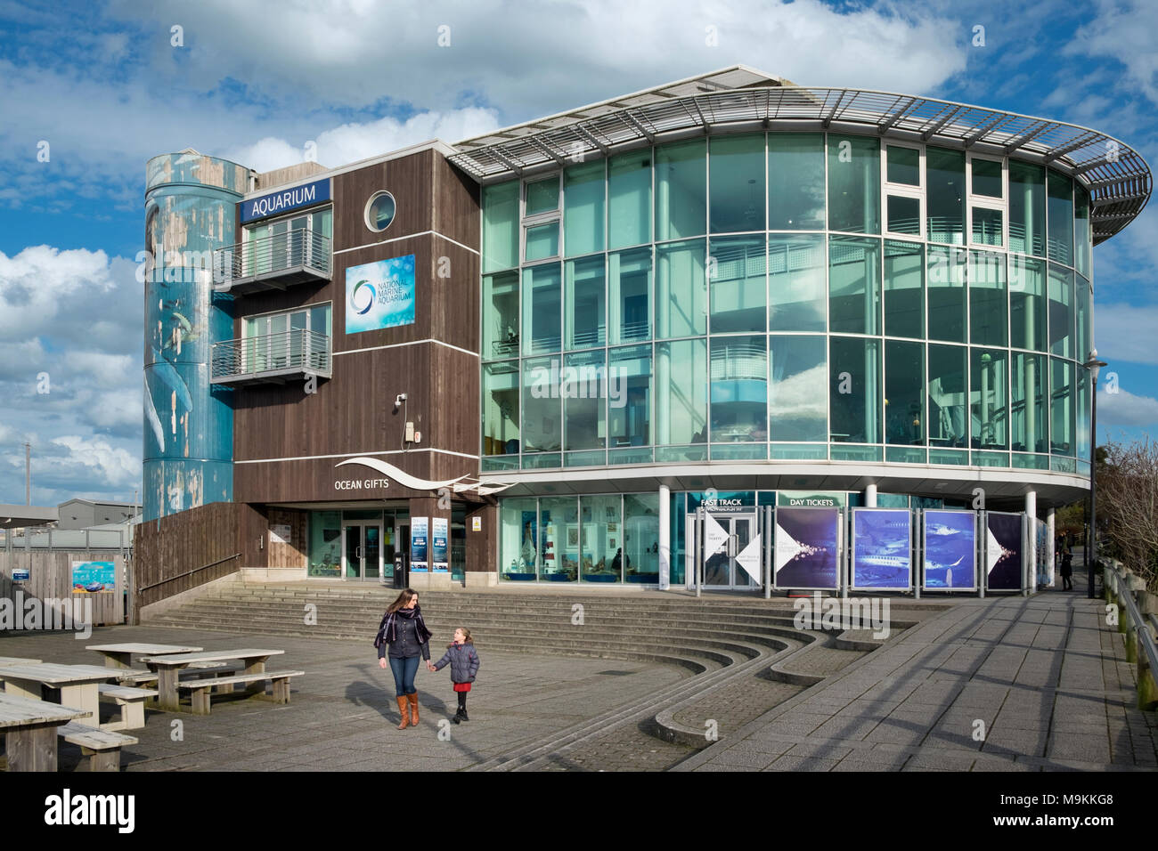 Eine Mutter und Kind zu Fuß entfernt von der National Marine Aquarium in Plymouth, Devon, UK an einem hellen, sonnigen Tag. Stockfoto