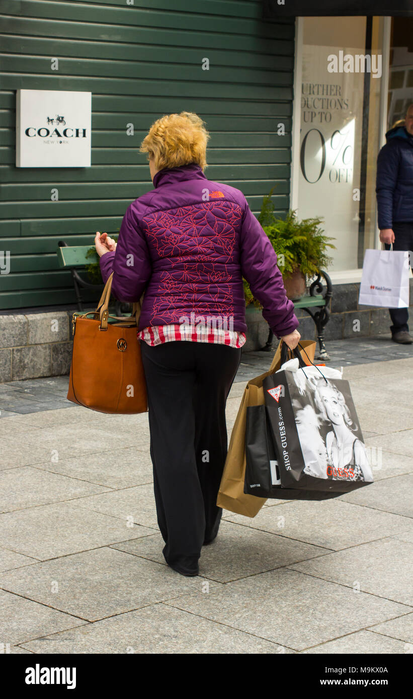 Eine Frau, die beladen mit Tragetaschen und genießen Sie einige retail Therapie am Markt Kildare Village Shopping Outlet in der Grafschaft Kildare, Irland Stockfoto