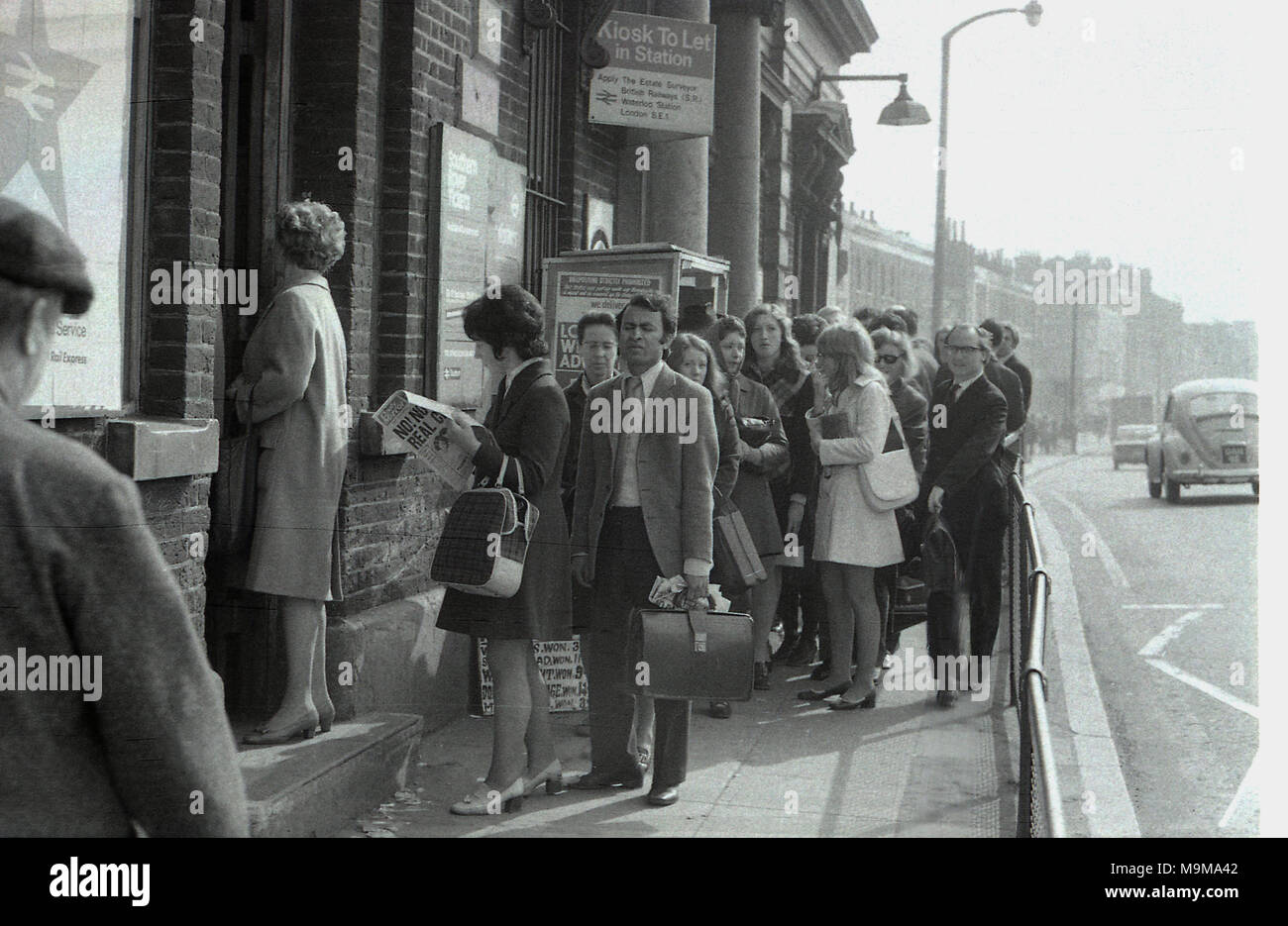 1970 s, historischen, Bahnreisende Schlange auf dem Bürgersteig außerhalb New Cross Bahnhof in South East London, England. Zu diesem Zeitpunkt, Streiks und abgebrochen Züge wurden ein gemeinsames Auftreten auf der British Rail und in diesem Fall die Plattformen waren zu voll, um mehr Fahrgäste zu nehmen. Stockfoto
