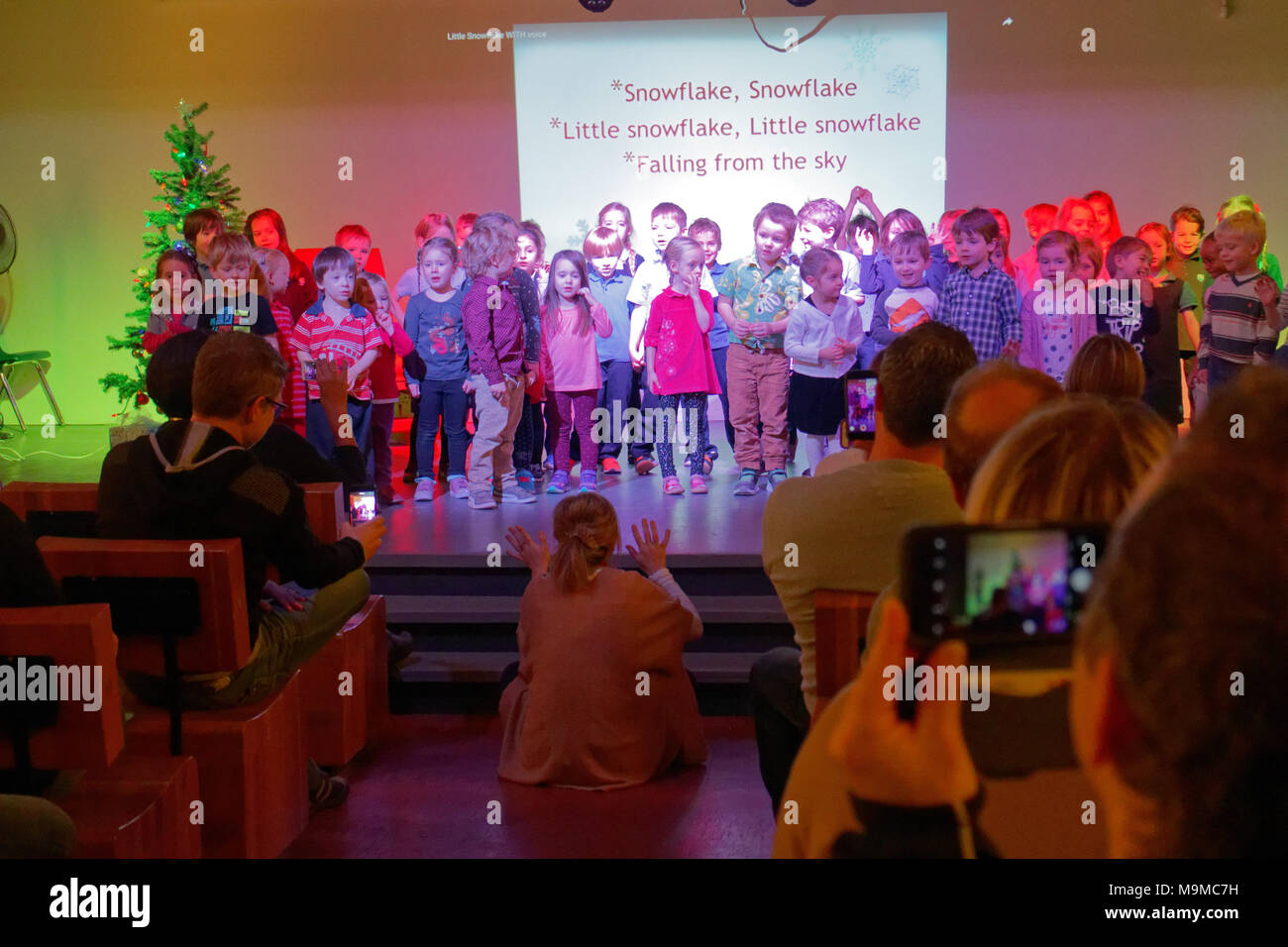 Kinder singen ihre Christmas Song auf der Bühne mit Eltern Filmen verwenden ihr Mobiltelefon Stockfoto
