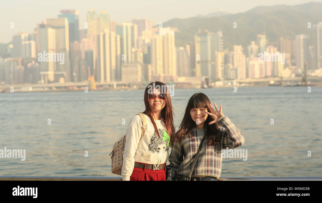 Hongkong, China - Januar 1, 2016: Zwei junge chinesische Touristen Mädchen Positiv posiert an der Küste in Hongkong, vor dem Hintergrund einer Stadt Panorama vom Victoria Harbour. Stockfoto