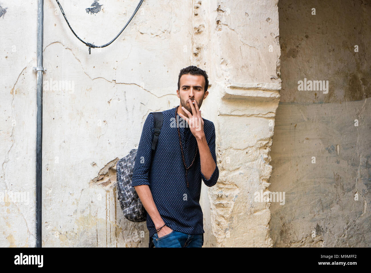 Junge muslimische Mann Rauchen einer Zigarette in Freizeitkleidung stehend durch die zerstörte Wand Stockfoto