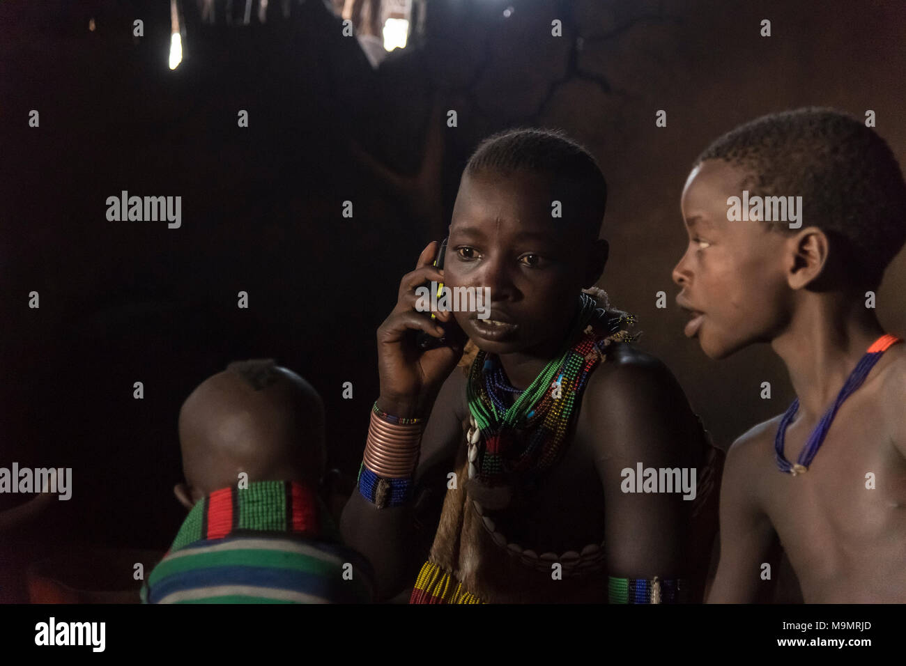 Junge Frau mit Kindern, Handy Anrufe in der Lehmhütte, Hamer Stamm, Turmi, Region der südlichen Nationen, Äthiopien Stockfoto