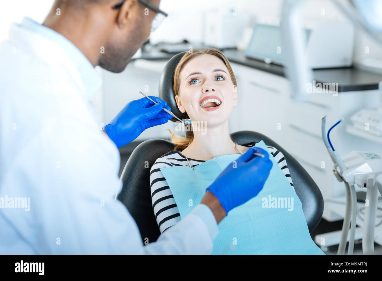 Dankbare Patienten. Angenehme junge Frau lächelte ihr männlichen Zahnarzt während der Vorbereitung für eine gründliche Untersuchung der Zähne und der Mundhöhle Stockfoto