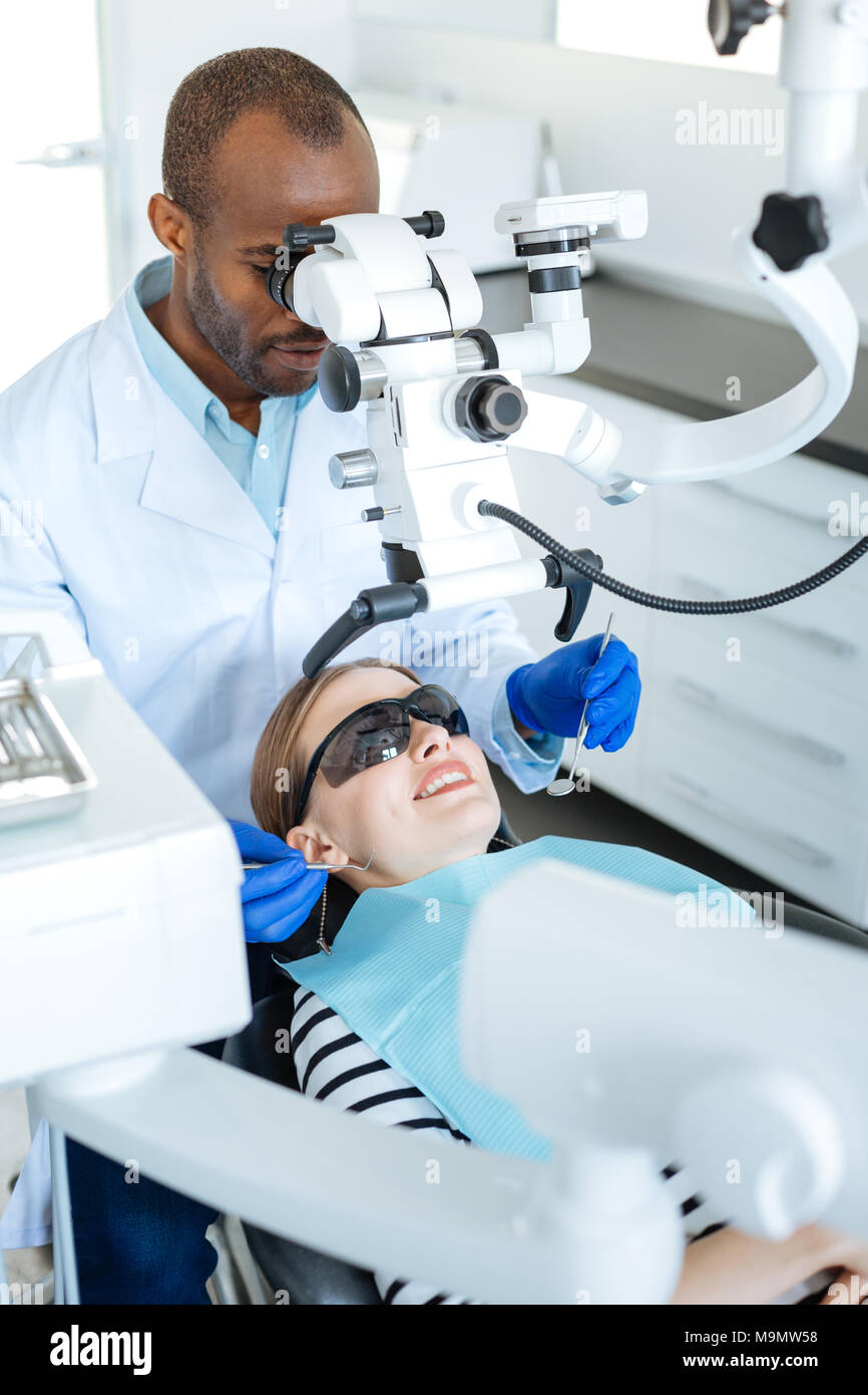 Hilfreiche Technologie. Qualifizierte junge männliche Zahnarzt Untersuchung der Mundhöhle seiner weiblichen Patienten und mit einem Mikroskop zu diesem Zweck Stockfoto