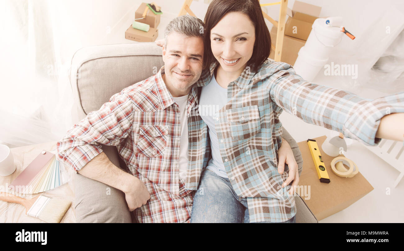 Glückliches Paar unter selfies zu Hause, während sie Haupterneuerungen, Sie sitzen auf einem Sessel und lächelnd Stockfoto