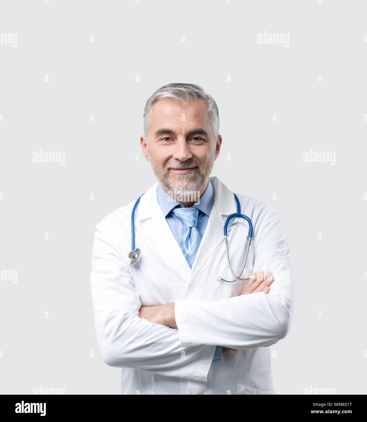 Zuversichtlich reife Arzt posiert mit verschränkten Armen, er lächelt an Kamera Stockfoto