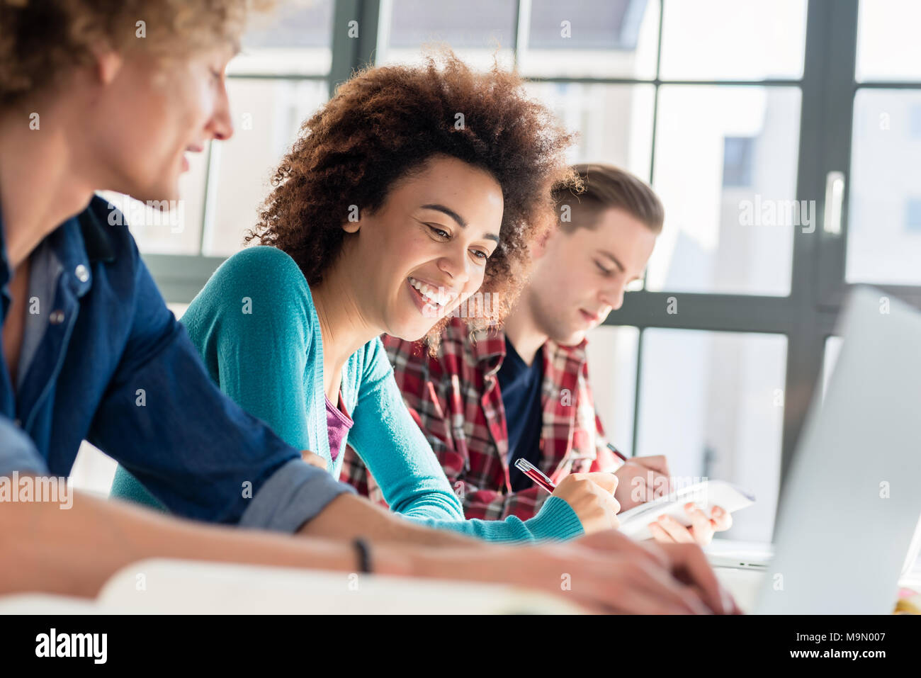 Fröhliche Frau schreiben eine Zuweisung während der Sitzung zwischen zwei Klassenkameraden Stockfoto