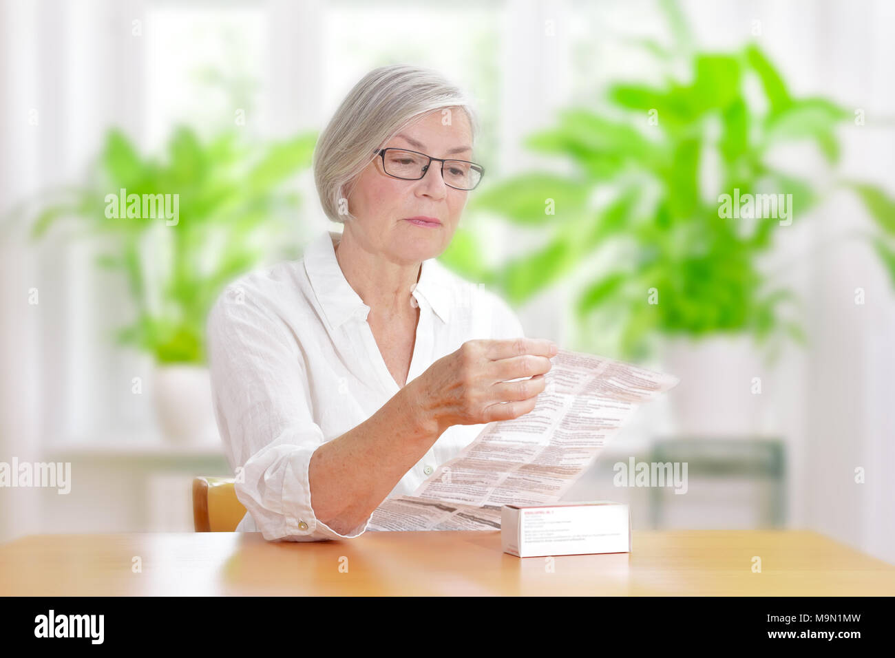 Ältere Frau an einem Tisch sitzen in Ihrem Wohnzimmer lesen der Information von Ihrem Arzt verschriebene Medikamente Stockfoto