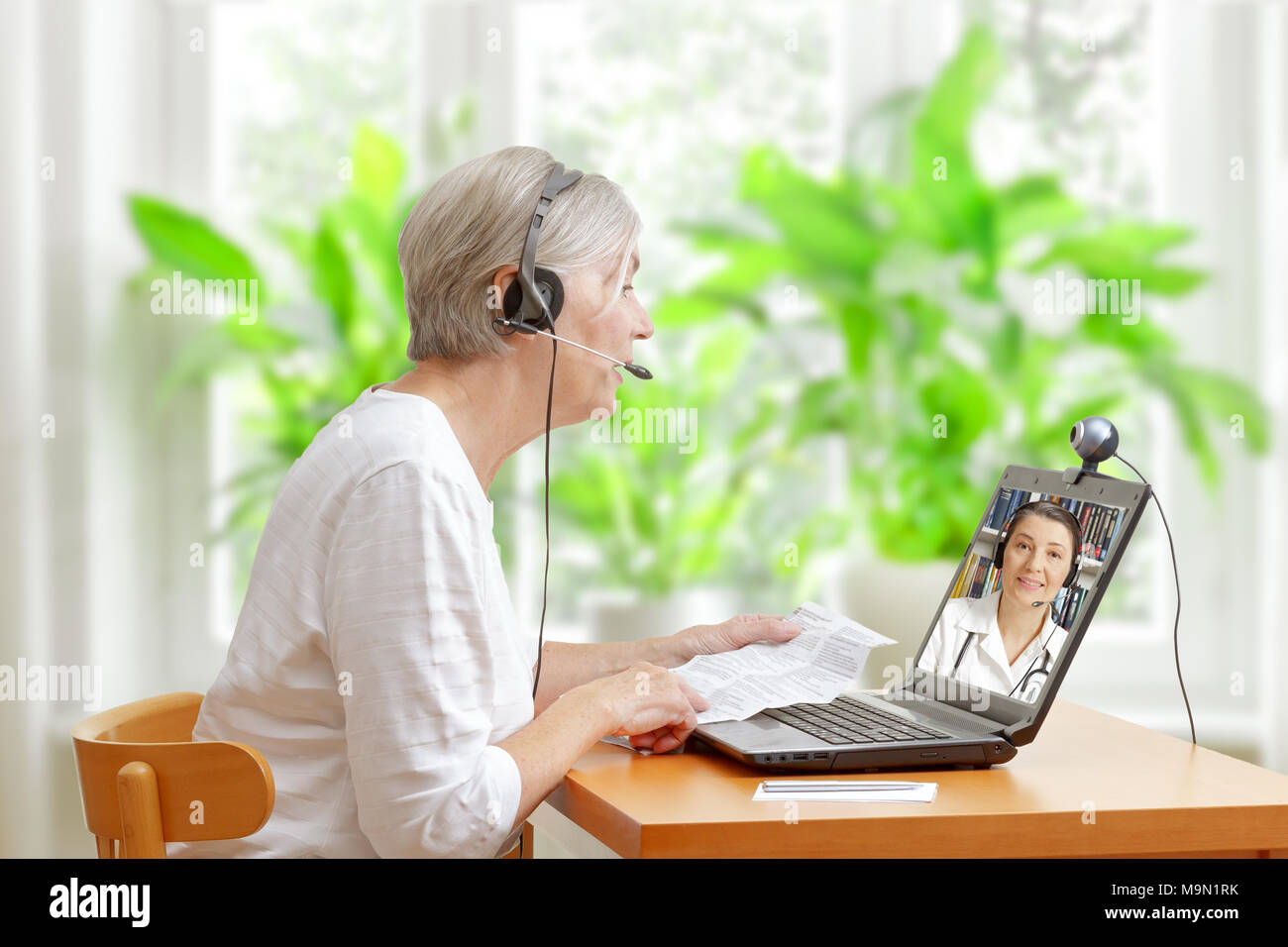 Ältere Frau an einem Tisch sitzen in Ihrem Wohnzimmer mit den Beipackzettel ihrer Medikamente während einer Videokonferenz mit Ihrem Arzt Stockfoto
