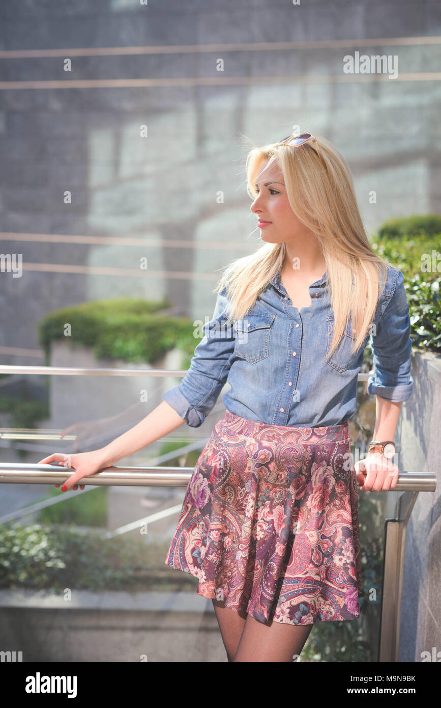 Junge schöne Blondine kaukasische Mädchen im Freien in der Stadt trägt eine Jeans Hemd und einem geblümten Rock weg schauen - Frische, Unbekümmertheit, Yout posing Stockfoto