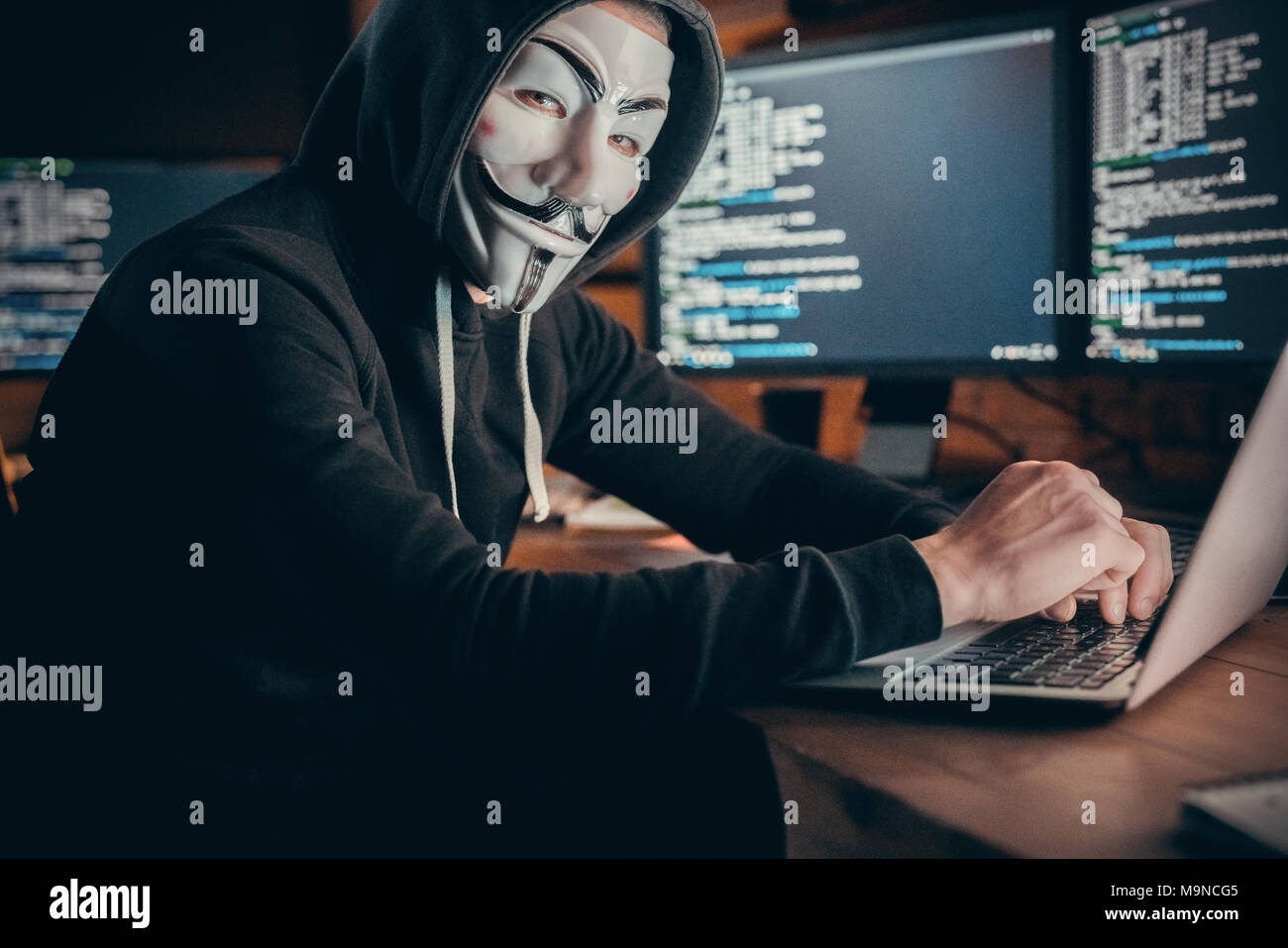 Maskierte hacker Sitzen am Arbeitsplatz im Rechenzentrum des Unternehmens. Innen-, Studio gedreht. Hackerangriffe, Viren, net-Konzept Stockfoto