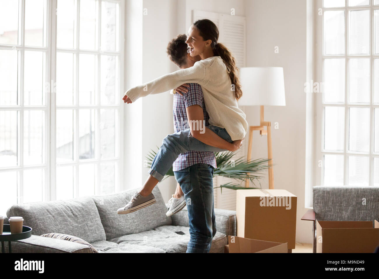 Aufgeregt Paar feiert bewegenden Tag, Mann anheben, die glückliche Frau ansehen unter Boxen froh ins neue Haus einziehen, Mann umarmt mich, w Stockfoto