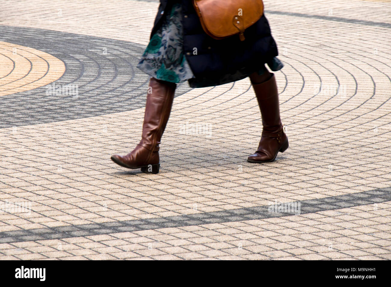 Die Beine einer Frau zu Fuß auf der Straße der Stadt konzentrische Kreise gepflasterten Fußgängerzone Pflaster in Bewegungsunschärfe Stockfoto