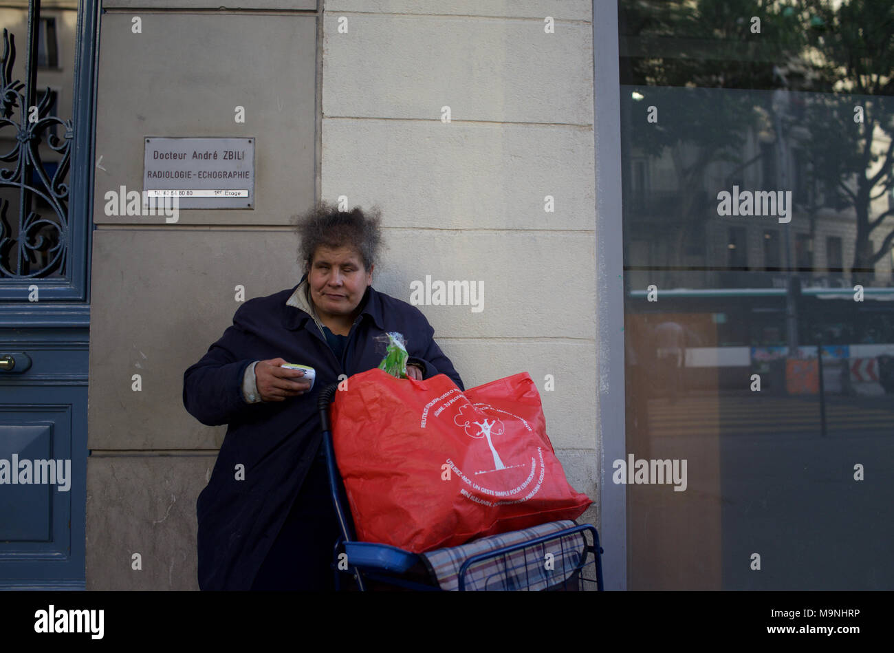 Obdachlose Frau sitzt auf der Straße mit großen roten Beutel - Boulevard Barbès, Paris, Frankreich Stockfoto