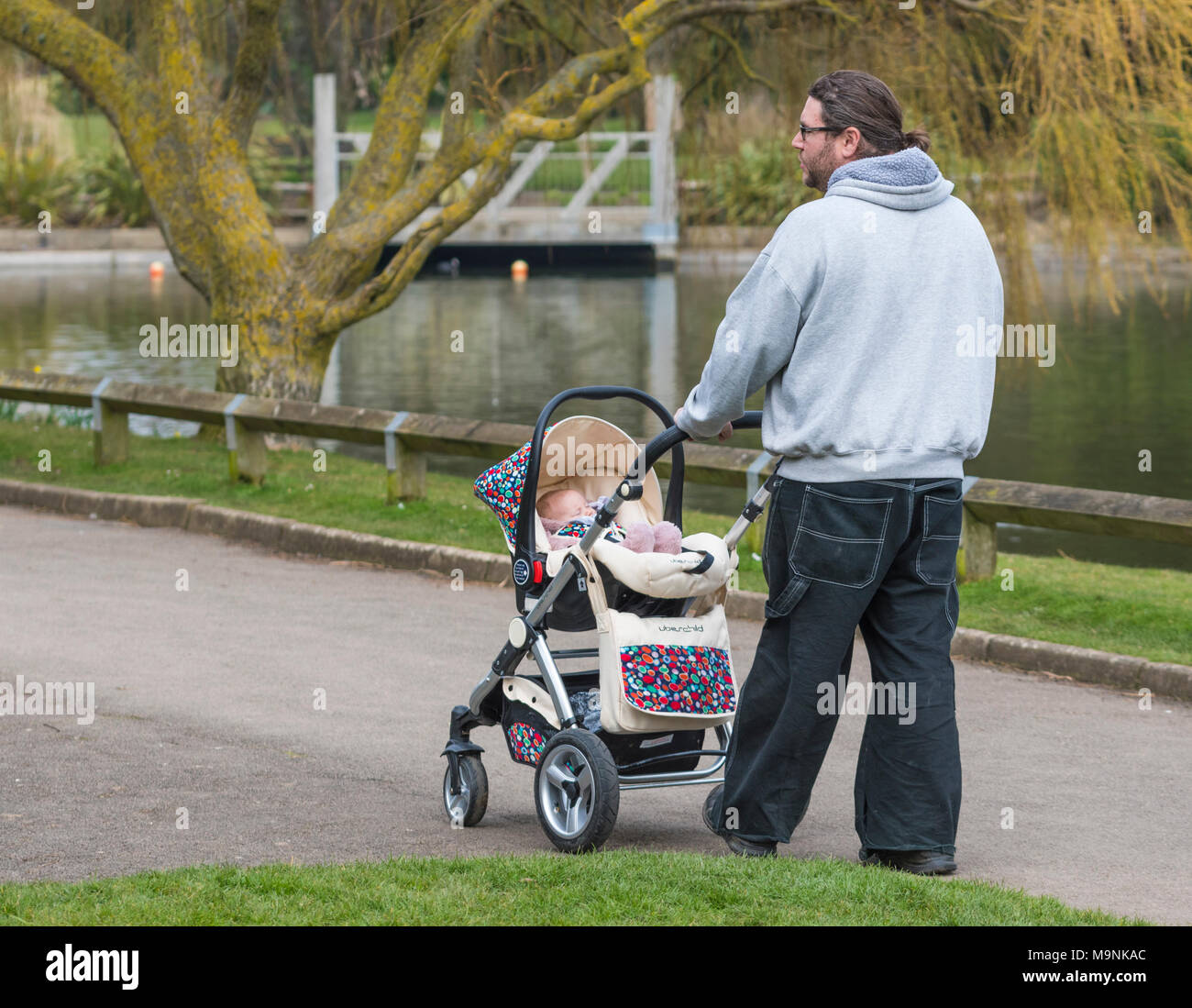 Man treibt ein Baby im Kinderwagen rund um einen See in einem Park in Großbritannien. Stockfoto