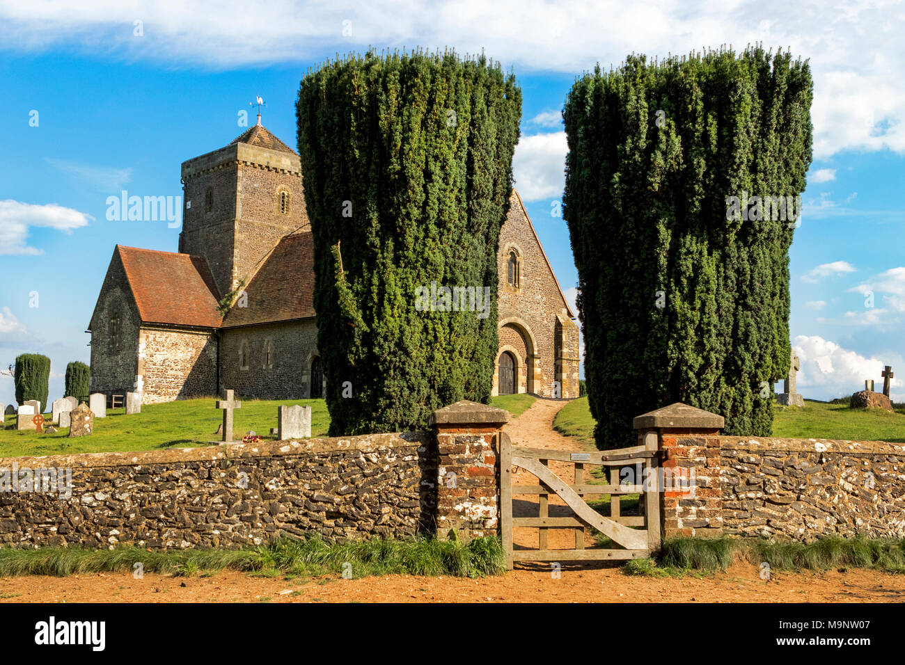 Eingang zur Kirche von St. Martha's Hill, flankiert von zwei Bäumen, mit einem blauen Himmel an einem sonnigen Tag in den North Downs mit Grabsteinen, Wand- und Gate Stockfoto