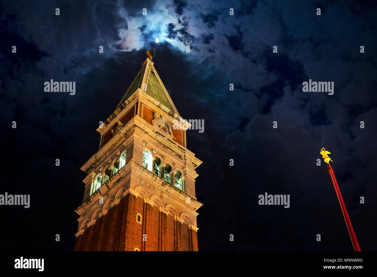 Der Campanile Auf dem Markusplatz in Venedig bei Nacht mit gold rot Fahnenmast kippte, beleuchtete Glockenturm und Pyramide Dach erreichen für den Mond Stockfoto
