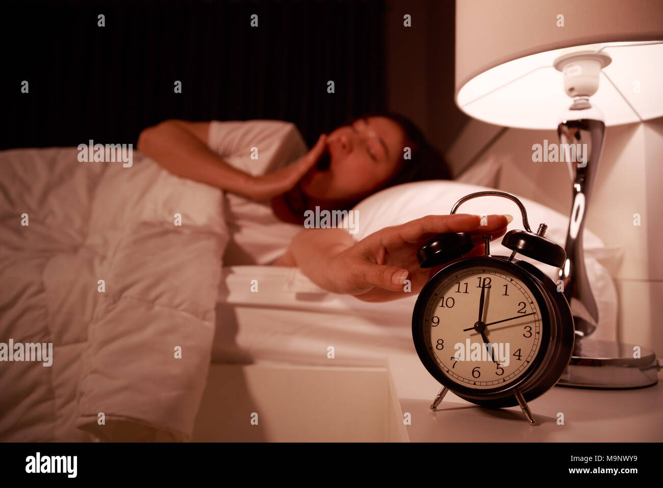 Verträumte junge Frau im Bett mit geschlossenen Augen Hand bis zum Wecker am Morgen Stockfoto