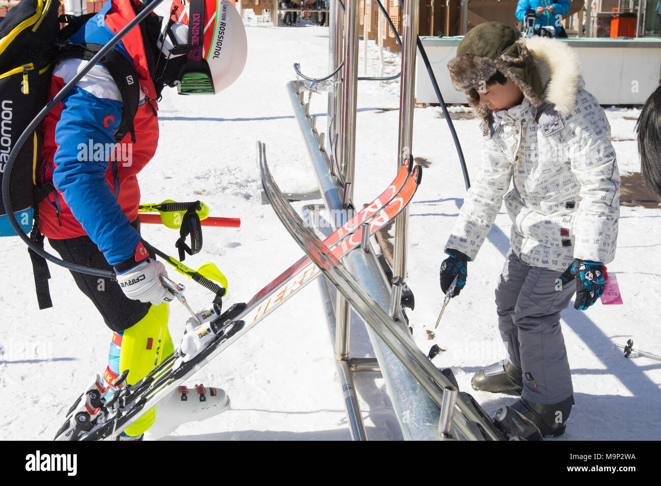 Zwei Kinder putzen Ihre Skier mit Druckluft Pistolen in der alpensia Resort, Region Gangwon-do, Südkorea. Die alpensia Resort ist ein Skigebiet und eine touristische Attraktion. Es ist auf dem Gebiet der Gemeinde von daegwallyeong-myeon befindet sich in der Grafschaft von Pyeongchang, die Olympischen Winterspiele hosting im Februar 2018. Das Skigebiet ist ca. 2,5 Stunden von Seoul oder Incheon Airport mit dem Auto, überwiegend alle Autobahn. Alpensia hat sechs Pisten für Ski und Snowboard, mit bis zu 1,4 km (0.87 mi) lang, für Anfänger und Fortgeschrittene, und einen Bereich für reserviert Stockfoto